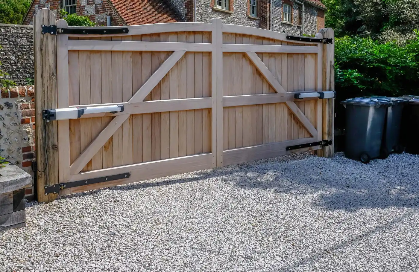Tall large wooden entry electric gates which are closed. Looking from the inside with a stone driveway in the foreground